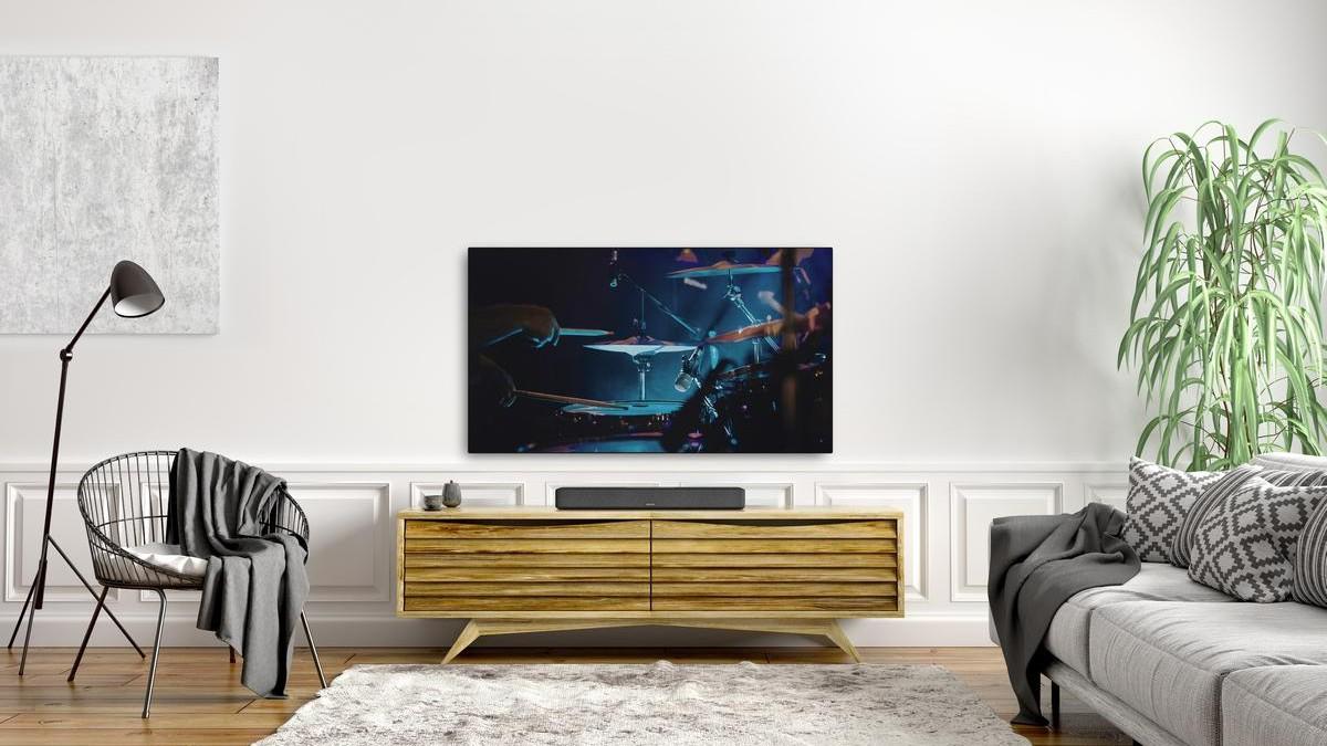 The Denon Sound Bar 550 sits in a comfortable room on a bamboo TV console beneath a mounted TV.