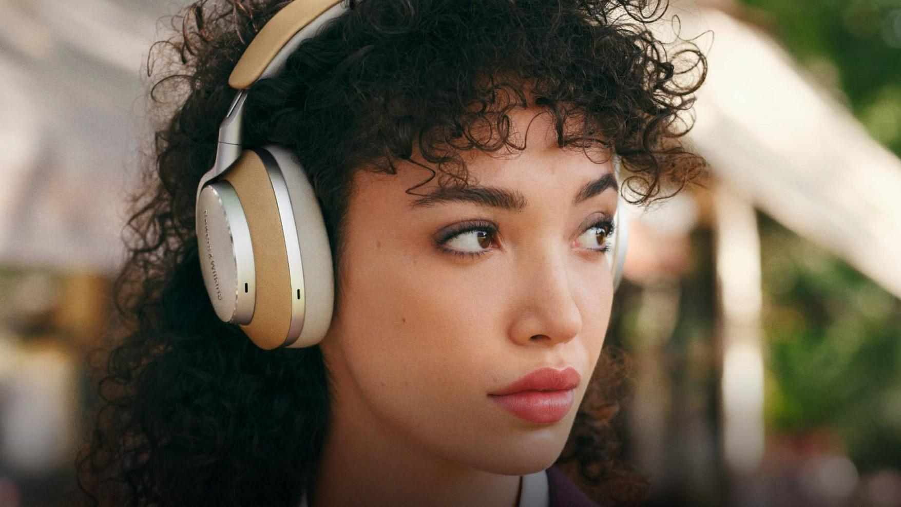A woman with curly black hair wears a white pair of the Bowers and Wilkins PX8 headphones