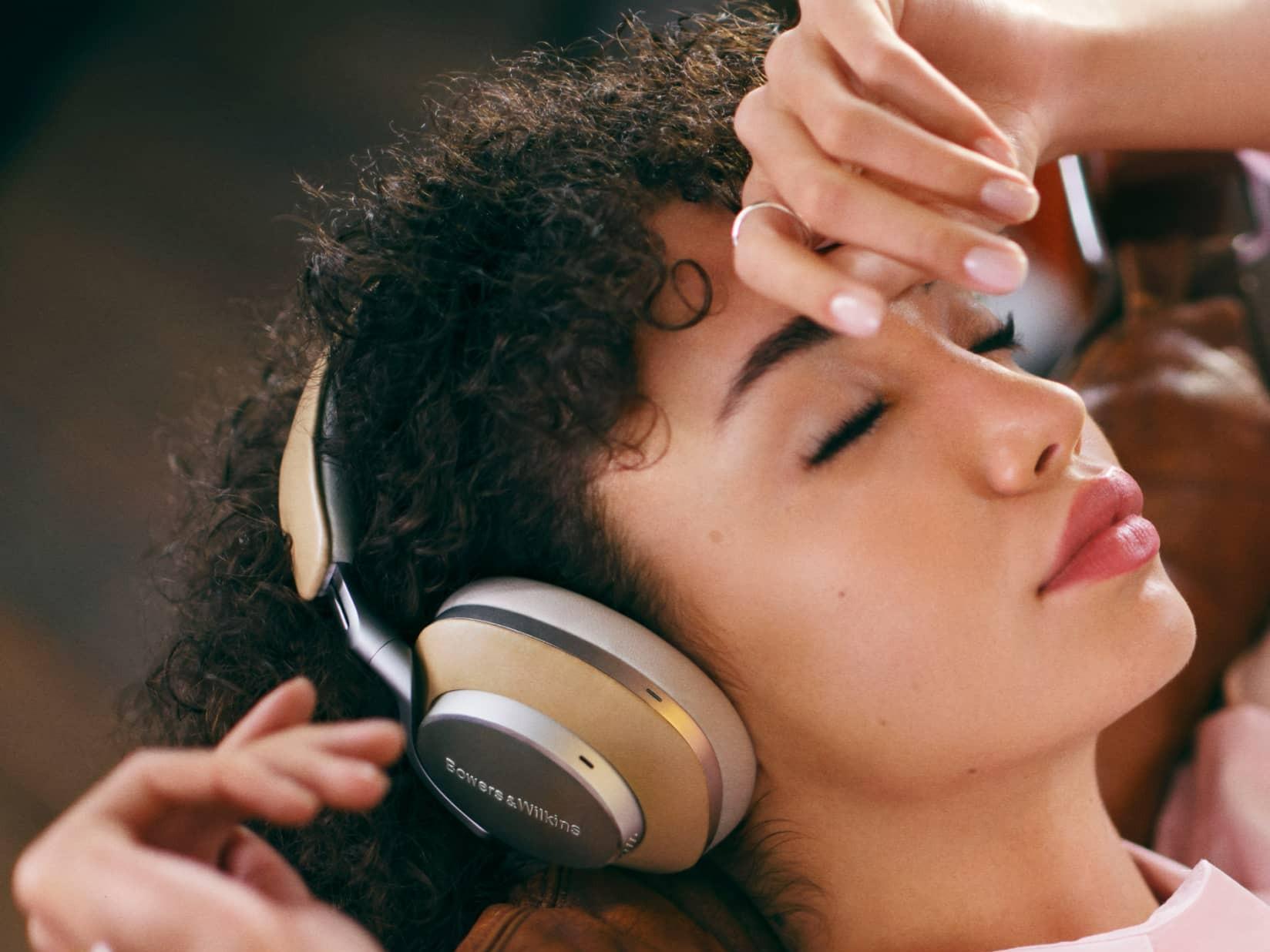 A woman with black curly hair listens with her eyes closed to the white model Bowers & Wilkins headphones