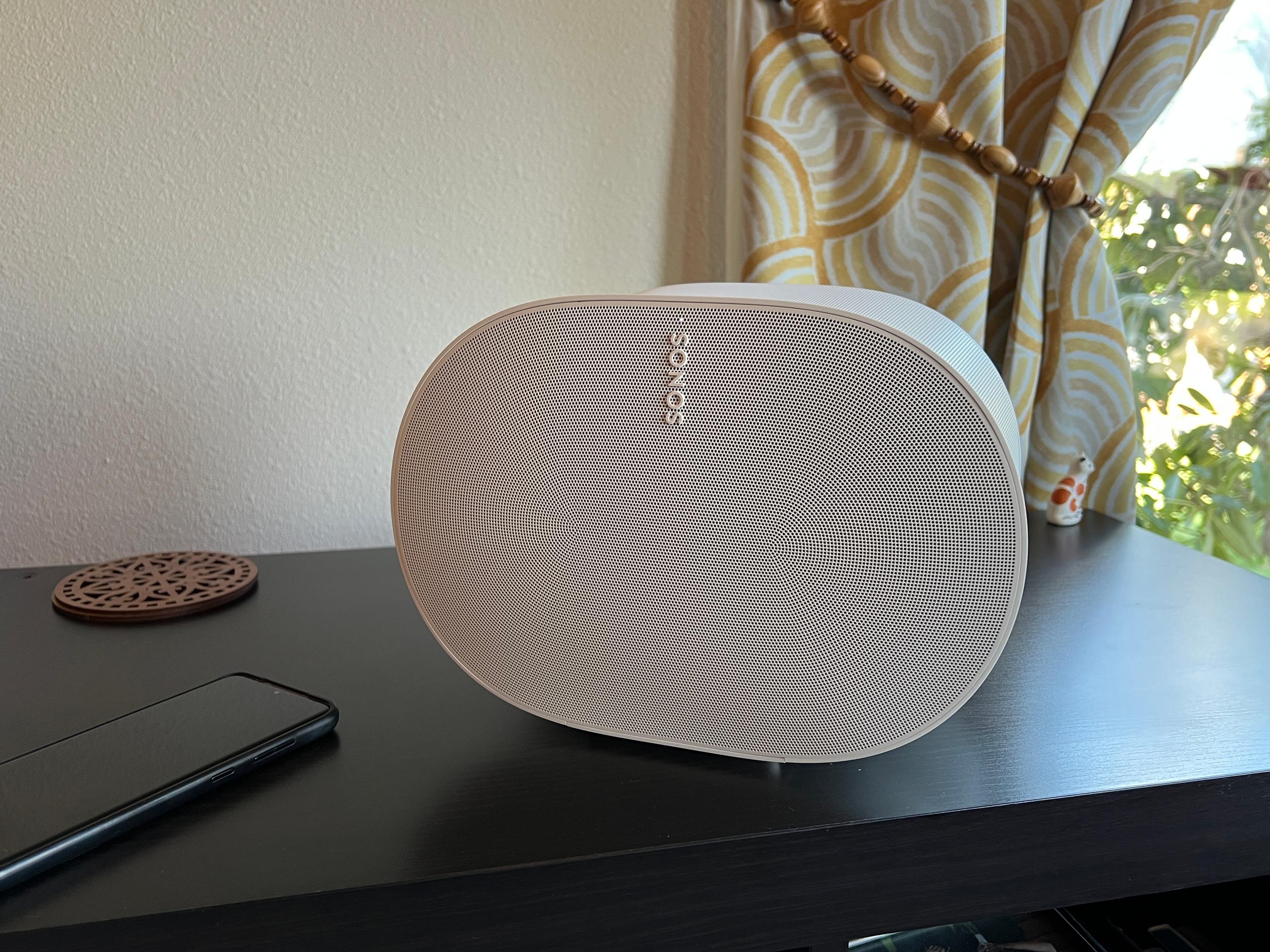 The Sonos Era 300 sits at an angle on a black record stand next to a phone.