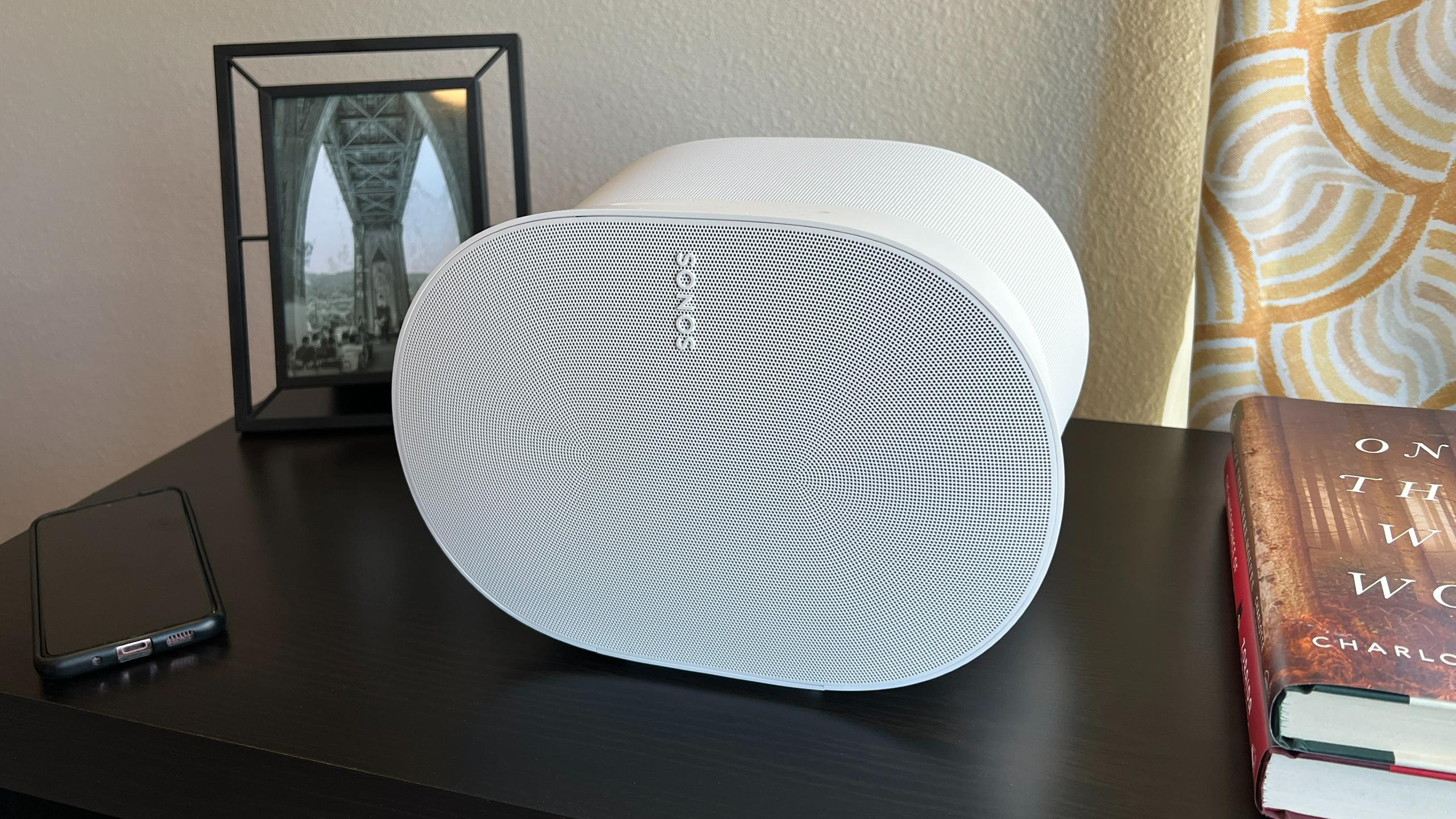 The Sonos Era 300 sits on a black record stand next to books and a phone.