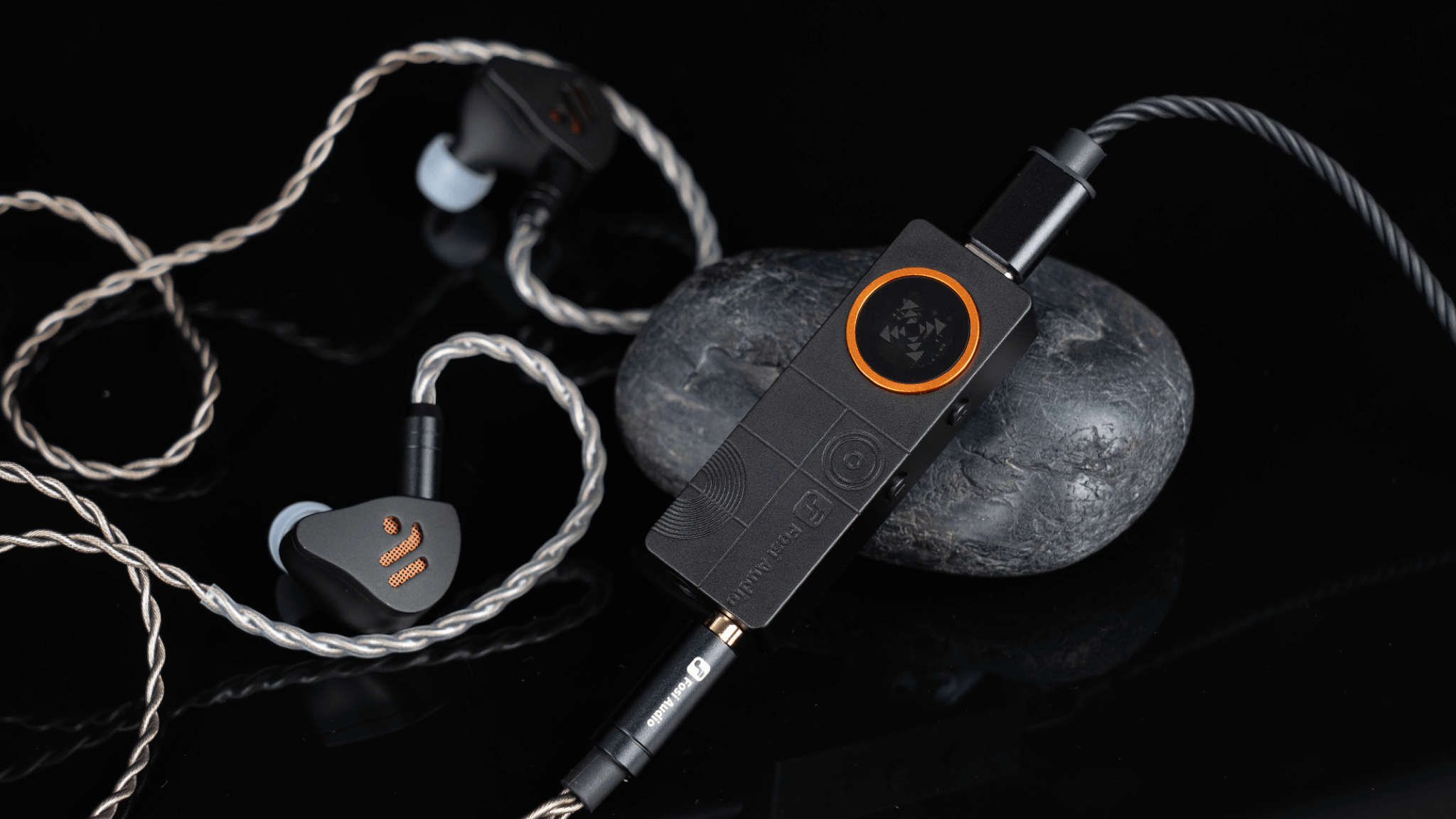 A close-up photo of the Fosi Audio DS3 portable DAC/amp connected to a pair of in-ear monitors
