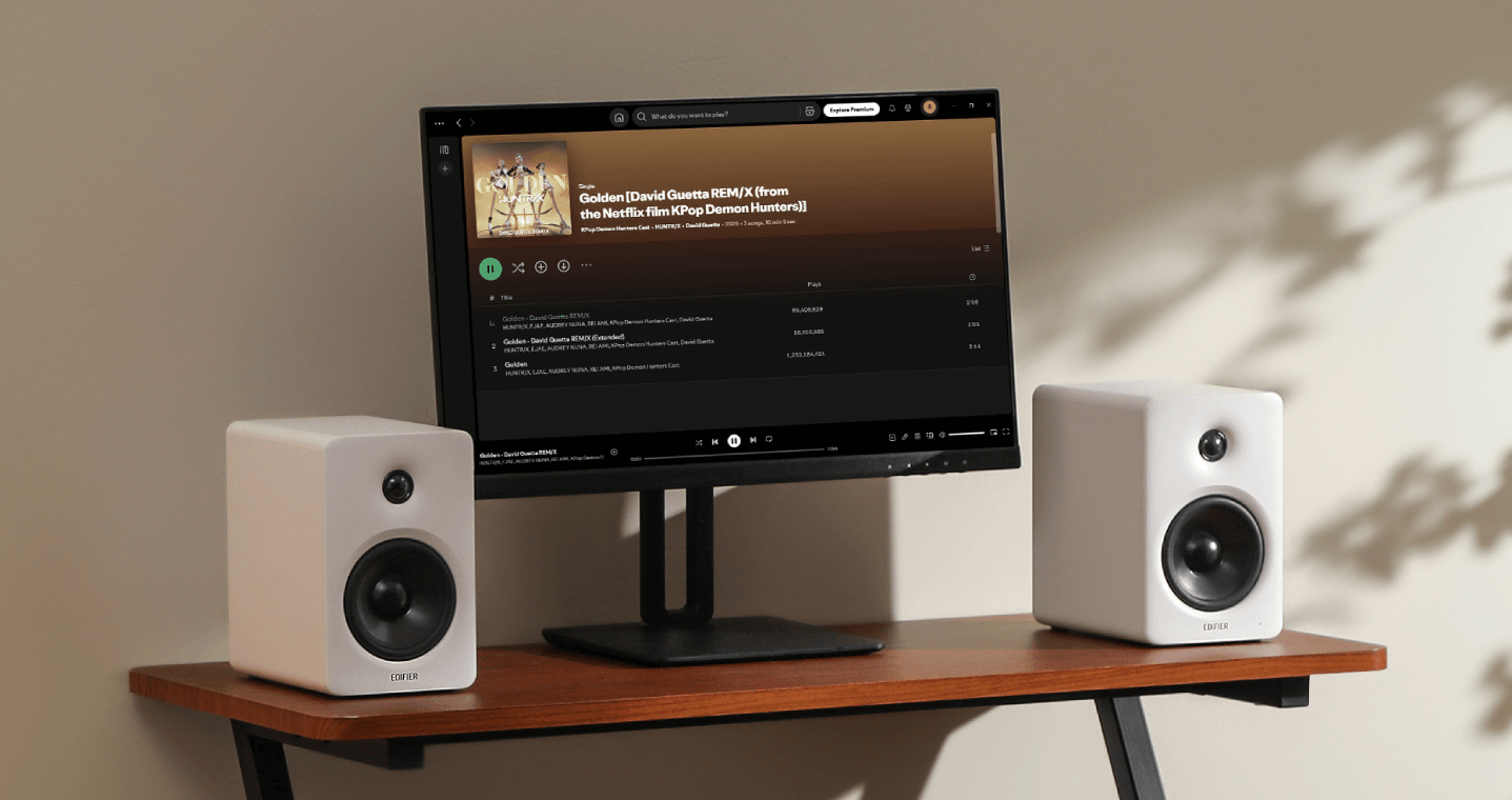 Two white Edifier M90 speakers placed on either side of a computer monitor playing music on a wooden desk.