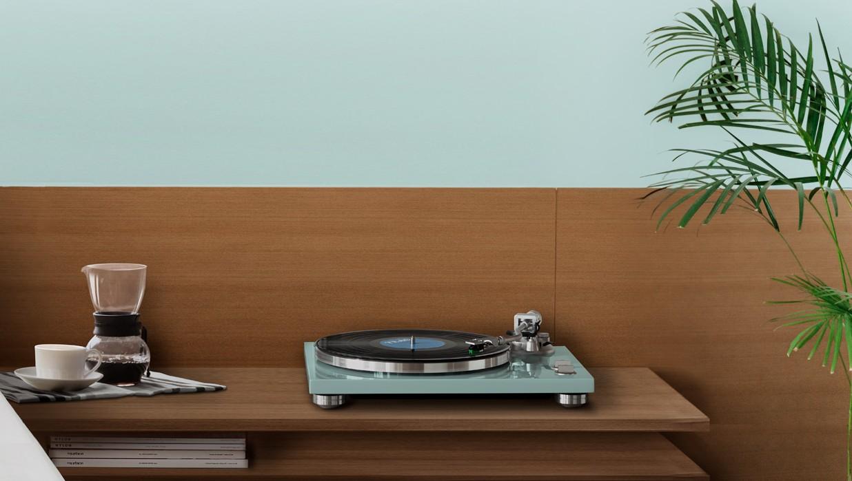 Turquoise TEAC TN-400BT X/TB turntable on a wooden shelf beside a coffee setup and a plant in a minimalist room.