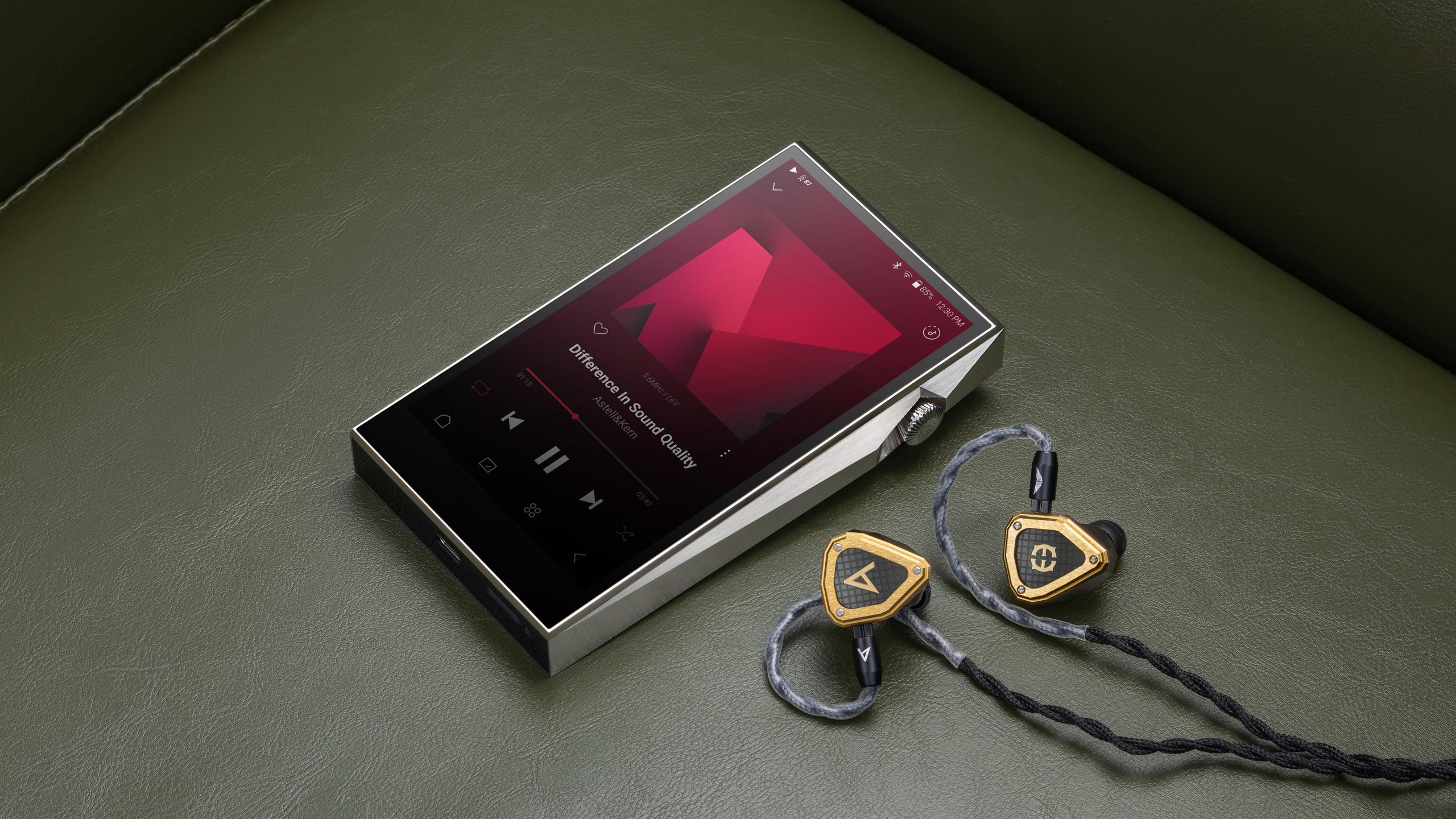High-end digital audio player with wired gold in-ear monitors on a green leather surface.