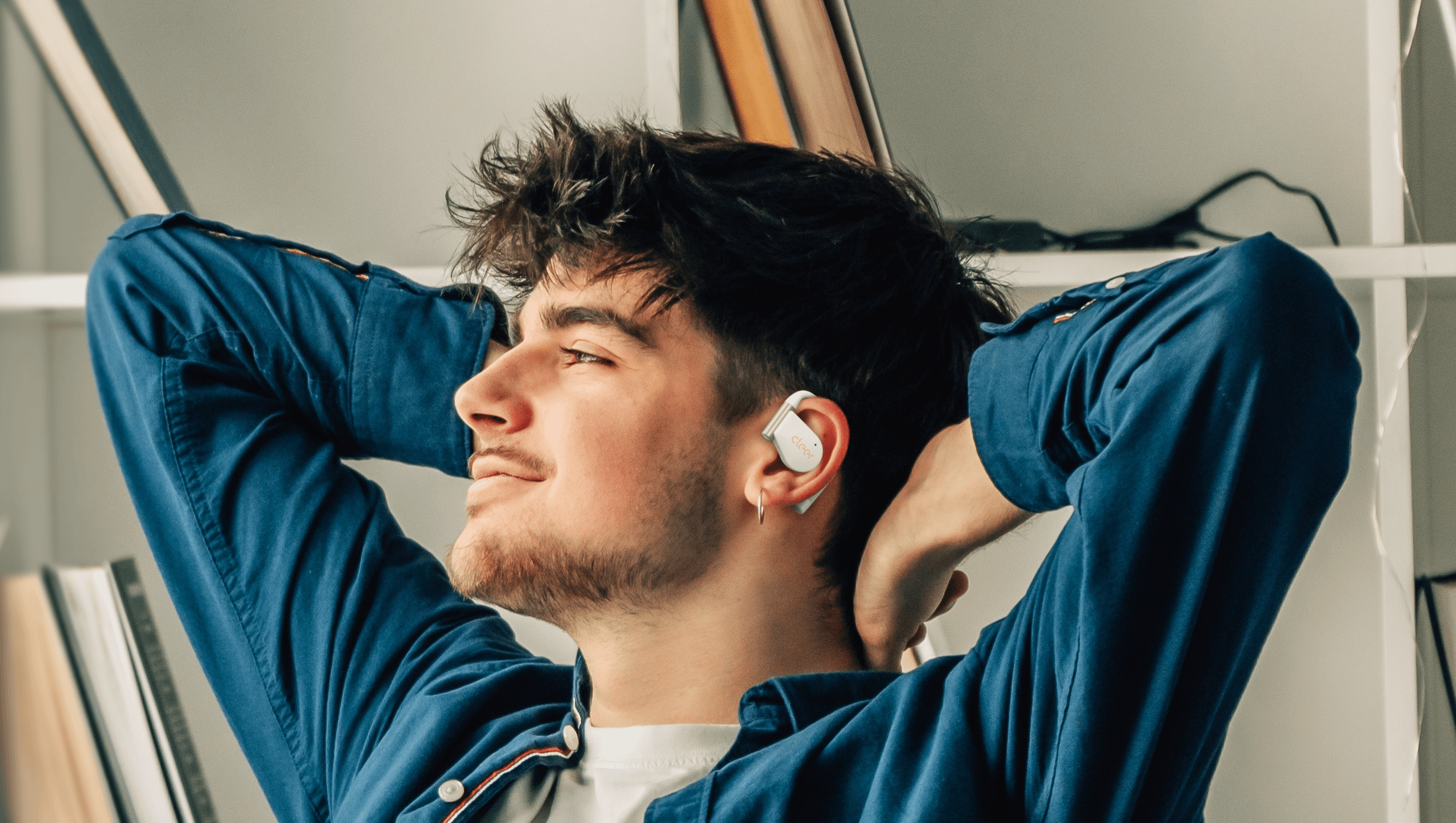 Man relaxing with Cleer ARC 5 open-ear earbuds in a home setting.
